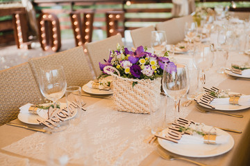 Coziness and style. Modern event design. Table setting at wedding reception. Floral compositions with beautiful flowers and greenery, candles, laying and plates on decorated table.