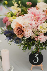 Coziness and style. Modern event design. Table setting at wedding reception. Floral compositions with beautiful flowers and greenery, candles, laying and plates on decorated table.