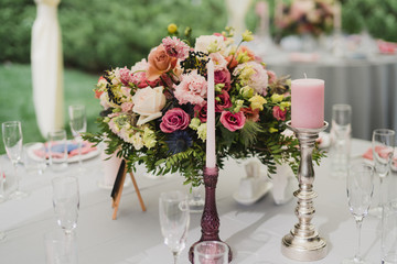 Coziness and style. Modern event design. Table setting at wedding reception. Floral compositions with beautiful flowers and greenery, candles, laying and plates on decorated table.