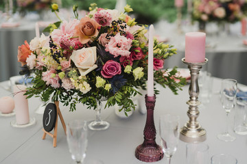 Coziness and style. Modern event design. Table setting at wedding reception. Floral compositions with beautiful flowers and greenery, candles, laying and plates on decorated table.