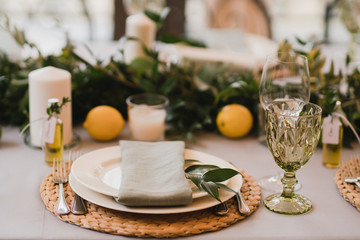 Coziness and style. Modern event design. Table setting at wedding reception. Floral compositions with beautiful flowers and greenery, candles, laying and plates on decorated table.