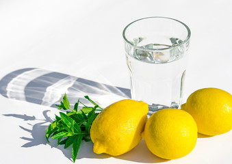 Lemons, fresh green mint and a glass glass with water on a white background