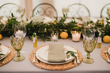 Coziness and style. Modern event design. Table setting at wedding reception. Floral compositions with beautiful flowers and greenery, candles, laying and plates on decorated table.