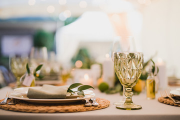 Coziness and style. Modern event design. Table setting at wedding reception. Floral compositions with beautiful flowers and greenery, candles, laying and plates on decorated table.