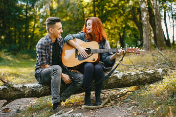 Cute couple in a park. Lady with red hair. Guy with a guitar