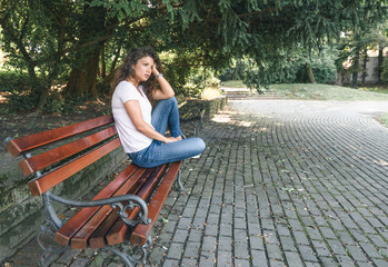 Young girl or woman sitting alone on the park bench feeling depressed and sad after she had argue...