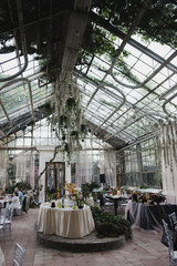 Coziness and style. Modern event design. Table setting at wedding reception. Floral compositions with beautiful flowers and greenery, candles, laying and plates on decorated table.
