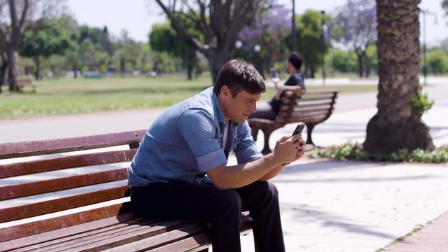 Frustrated man smashes his phone on a bench and throws it.