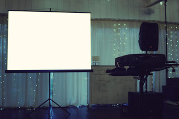 Empty projection screen put in the centre of a illuminated stage in a banquet hall. Projection...
