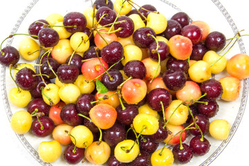 Cherry berries cherries red pink yellow with cuttings leaves with water droplets on a plate. Food ecology and agriculture.