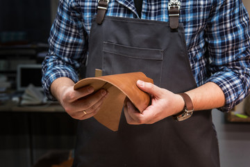 Man with leather textile at a workshop. Closeup. Concept of handmade craft production of leather goods.