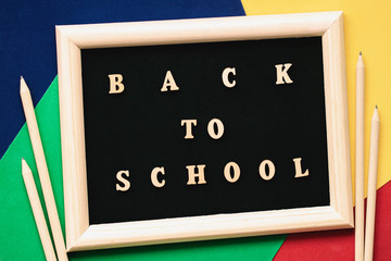 Back to school text, wooden letters in black background, frame on colored paper sheets, pencils. Concept of education, starting school
