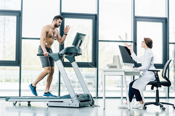 doctor sitting at computer desk and conducting endurance test with sportsman in gym
