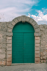 Green arched door in a stone fence against a blue sky