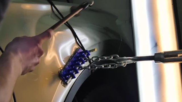 PDR. Paintless Dent Repair Removal. A man knocks on a car with a steel hammer to level a dent. Close-up metal keys, adhesive tabs, tools, aesthetic, leveling technology without painting