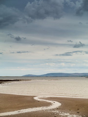 S shaped stream flows into ocean, Calm simple scene, Galway bay, cloudy sky, Vertical image. Pastel color