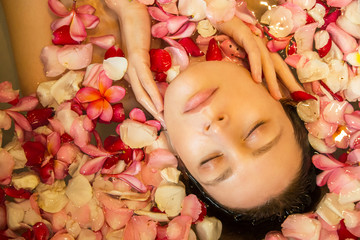 Fototapeta na wymiar Portrait of beautiful young woman in the bathtub full of frangipani petals, natural look, bare skin with no make up