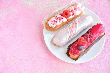 Tasty French eclairs cake with creative pink decor and fresh berries on pink textured table. Selective focus. Delicious dessert profiteroles with pink and red icing and sugar decor elements. 