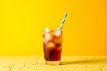 Glass with cold cola and tubule against yellow background - obrazy, fototapety, plakaty
