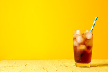 Glass with cold cola and tubule against yellow background