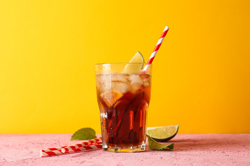 Glass with cold cola, tubule and lime slice against yellow background