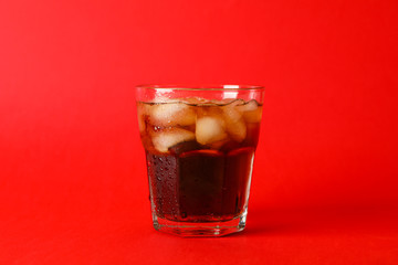 Glass of cold cola on red background, space for text