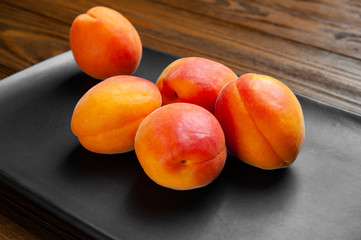 Apricots on a dark background. A pile of fresh juicy ruddy apricots piled in a dark clay plate on a wooden table.