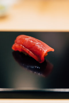 Japanese Omakase meal: Close up Chutoro (Bluefin Tuna) Sushi served by hand with pickled ginger on glossy black plate. Japanese luxury meal.