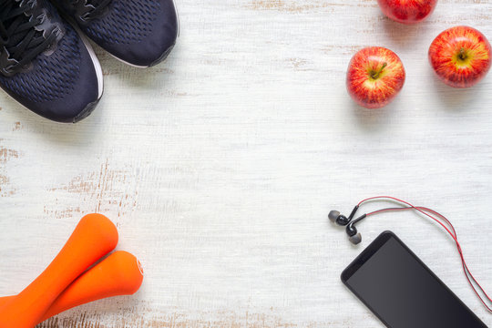 Top view of Active healthy fitness and workout lifestyle background concept, sport shotes, dumbbells, smartphone and apples on grunge white wood  background with copy space. Flat lay.