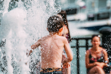 The child plays in the fountain in the hot summer