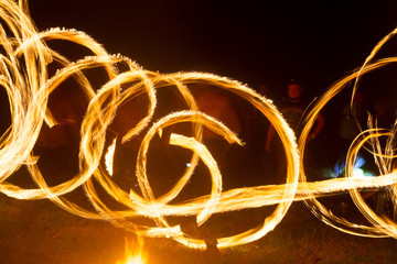 The artist shows a fire show at night spinning torches, circles of fire and loops