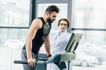 Fototapeta na wymiar sportsman training on treadmill near doctor during endurance test in gym