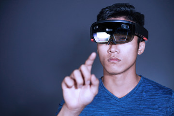 The Asian young man with glasses of virtual reality. Experience VR hololens headset in studio with advanced technology.