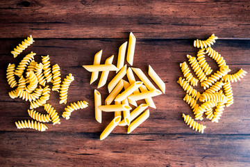 Variety of types and shapes of dry Italian pasta - fusilli and penne, top view. Uncooked whole wheat italian pasta. Image with copy space. 