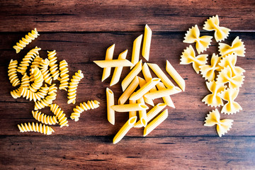 Variety of types and shapes of dry Italian pasta - fusilli, farfalle or bow tie pasta and penne, top view. Uncooked whole wheat italian pasta. Image with copy space. 
