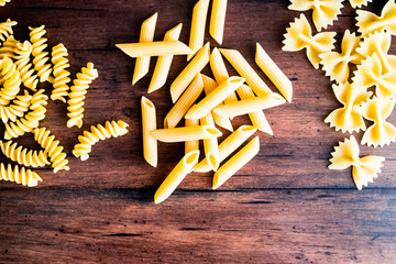 Variety of types and shapes of dry Italian pasta - fusilli, farfalle or bow tie pasta and penne, top view. Uncooked whole wheat italian pasta. Image with copy space. 