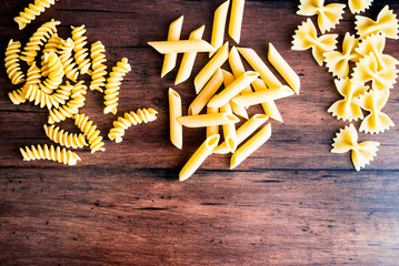 Variety of types and shapes of dry Italian pasta - fusilli, farfalle or bow tie pasta and penne, top view. Uncooked whole wheat italian pasta. Image with copy space. 