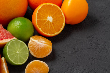 group of whole and sliced citrus fruits - tangerines, lemons, limes, oranges, grapefruits on the surface of the dark table - image with copy space