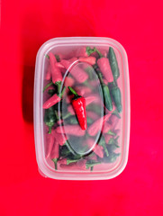 Red and green chilli peppers. Close up over head view of the freshly picked chillies in a plastic storage box. Red background.