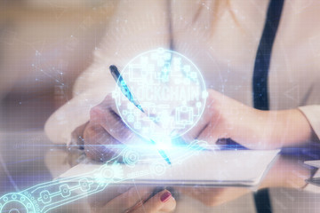 Cryptocurrency hologram over woman's hands writing background. Concept of blockchain. Double...