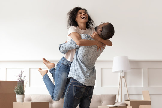 African husband lifting happy wife celebrating moving day with boxes