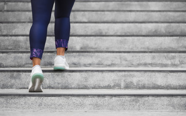 Fototapeta na wymiar Female runner athlete doing a stairs climbing. Running woman doing run up steps on staircase in urban city. Doing cardio sport workout. Exercise outside in summer. Activewear leggings and shoes.