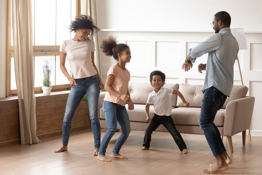Happy funny active african family of four dancing at home