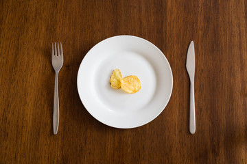 Potato chips on white plate on wood table with knife and fork