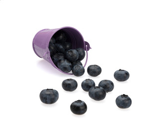 Berries of ripe blueberries (blueberries) in a lilac overturned bucket, and scattered around it, on a white background. Close-up. Still life.