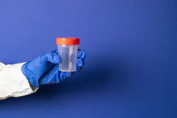Doctor's hand in latex blue gloves holds a plastic container with biological material