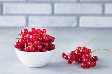 Fresh red currants in a white bowl on a gray background.