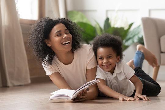 African mom reading book laughing with child son at home