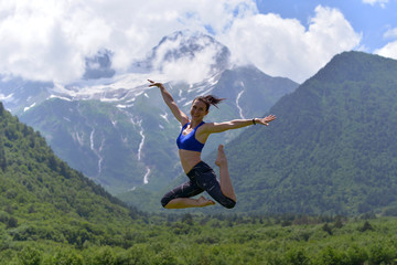 Young sports woman doing yoga on the green grass in the summer on the background of snowy mountains.