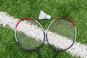 Red badminton rackets and shuttlecock lie on the artificial grass of a sports stadium. Amateur badminton set. Concept of summer hobby, outdoor sports, entertainment. Place for text, flat lay.